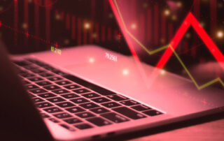 Laptop met rode neerwaartse pijl en dalende beursgrafiek die een negatieve markttrend visualiseert.
