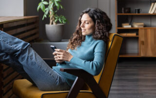 Vrouw zit ontspannen in een stoel met haar voeten omhoog terwijl ze haar smartphone gebruikt, om te beleggen of de markt te analyseren.